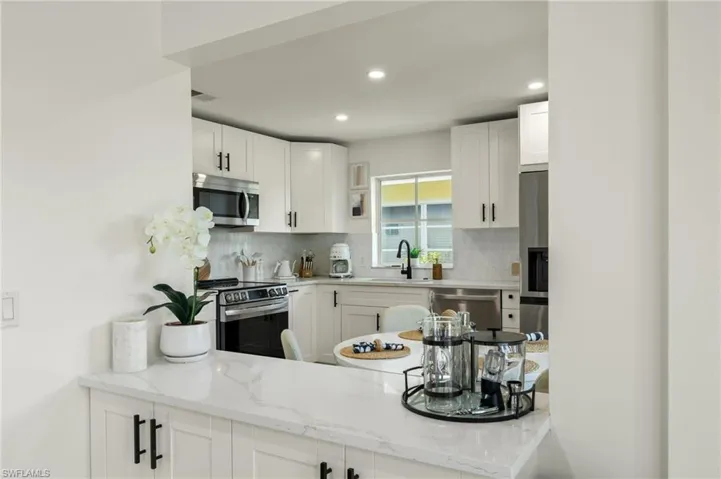 Kitchen featuring white cabinetry, sink, light stone counters, and appliances with stainless steel finishes