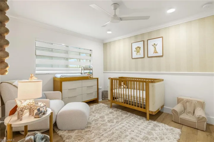 Bedroom with ceiling fan, light wood-type flooring, a nursery area, and ornamental molding