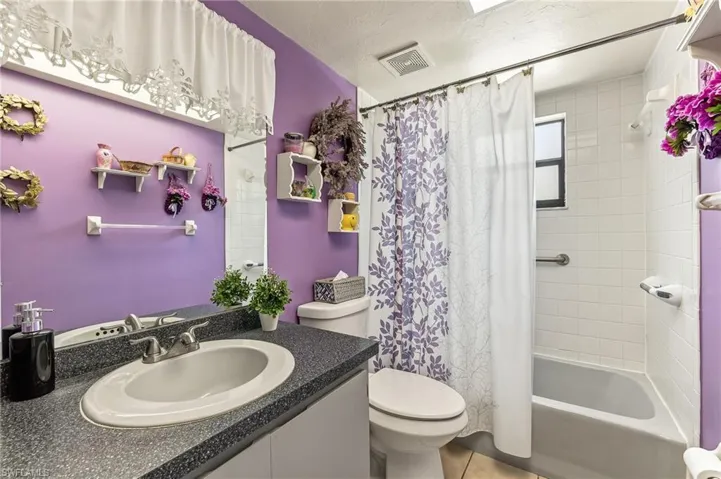 Bathroom featuring a single vanity with a speckled countertop and an oval undermount sink, a toilet, and a shower-over-tub combination with white tile surround