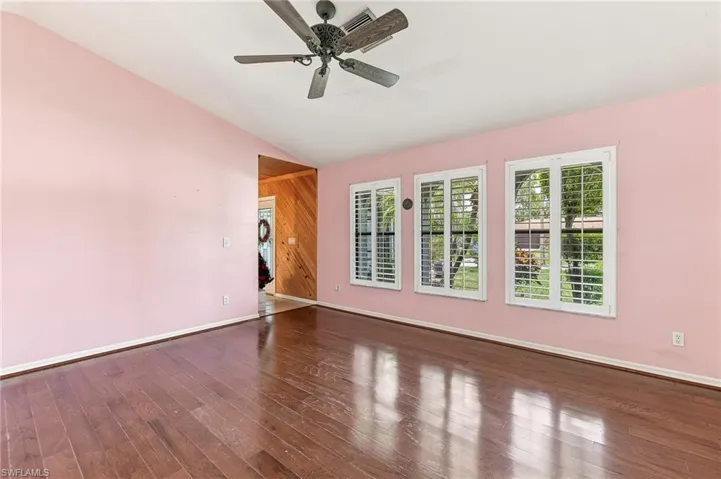 Vaulted ceiling room featuring rich wood flooring and three large windows with white louvered shutters