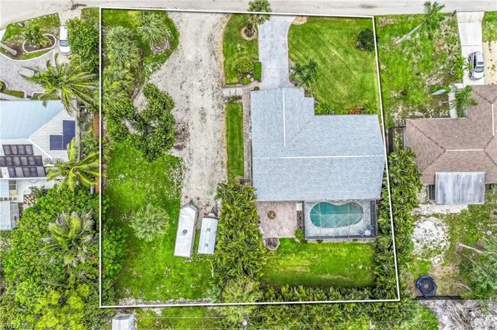 Aerial view of a property featuring a single-story residence with a gray shingle roof, a kidney-shaped swimming pool with a screened enclosure, a paved driveway, and expansive green lawns