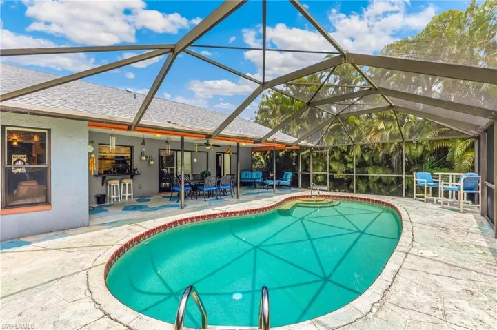 Screen-enclosed pool area featuring a freeform pool with blue tile border, surrounding textured patio, and an outdoor bar with built-in countertop