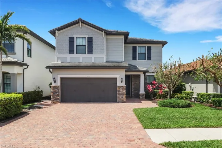 View of front of property featuring a garage, stone siding, a tile roof, and decorative driveway