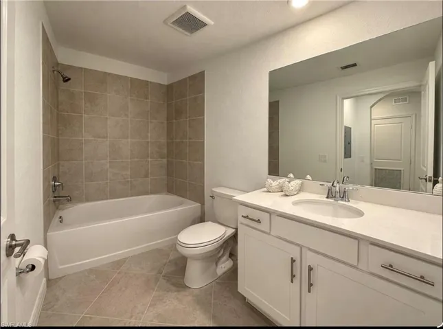 Bathroom featuring a white vanity cabinet with a light-toned countertop, an integrated oval sink, a large wall-mounted mirror, a tub-shower combination with tile surround, and tile flooring
