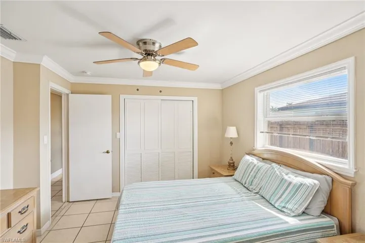 Bedroom with crown molding, ceiling fan, light tile patterned floors, and a closet