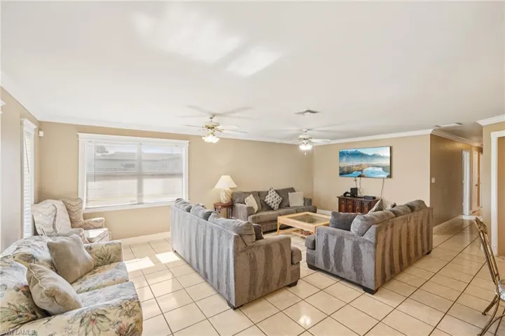 Living room with crown molding, light tile patterned floors, and a ceiling fan