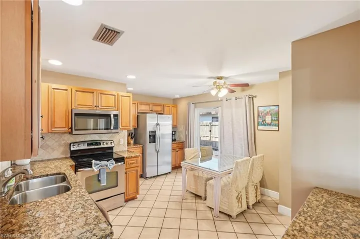 Kitchen featuring stainless steel appliances, a ceiling fan, light stone counters, light tile patterned flooring, and recessed lighting