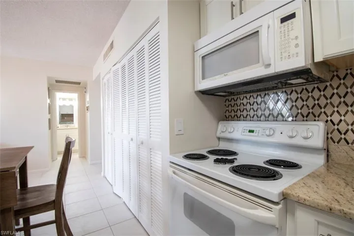 Kitchen with white appliances, light tile patterned floors, white cabinetry, a textured ceiling, and tasteful backsplash