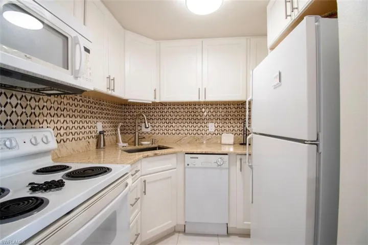 Kitchen featuring white appliances, white cabinets, light stone countertops, backsplash, and light tile patterned floors