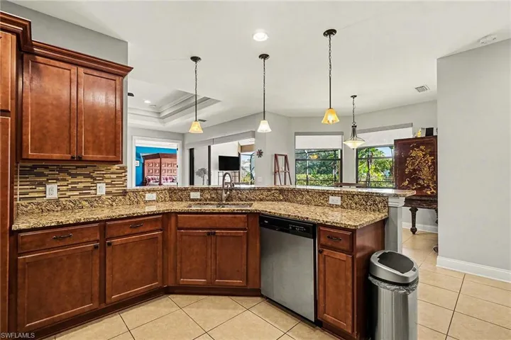 Kitchen with stainless steel dishwasher, light stone counters, hanging light fixtures, light tile patterned floors, and recessed lighting