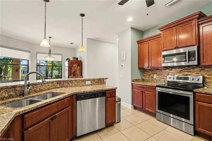 Kitchen with appliances with stainless steel finishes, light stone countertops, backsplash, hanging light fixtures, and light tile patterned floors