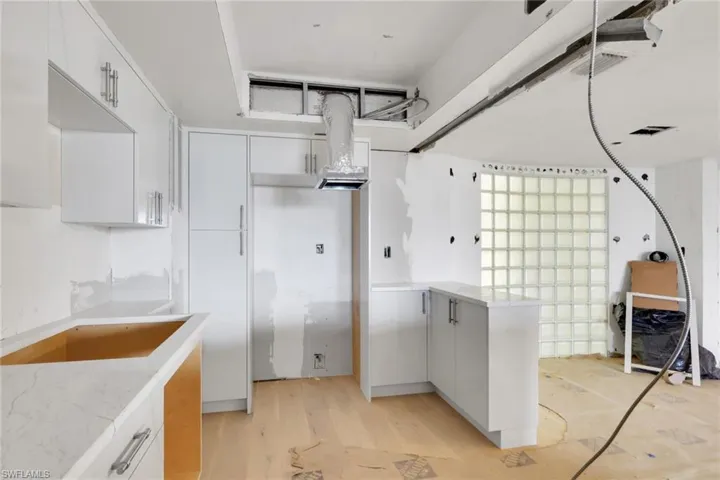 Kitchen with white cabinetry, light wood-type flooring, a peninsula, and light stone counters