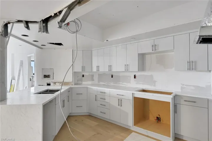 Kitchen featuring white cabinets, ventilation hood, a peninsula, light wood-style floors, and light stone counters