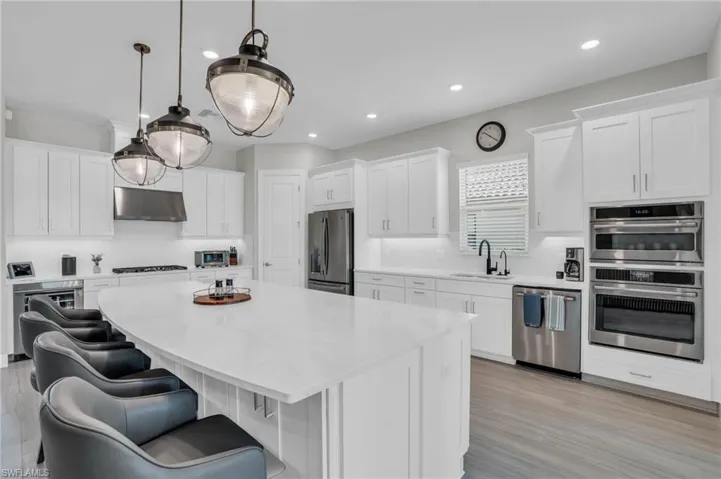 Kitchen with stainless steel appliances, light wood-type flooring, a kitchen island, sink, and white cabinetry