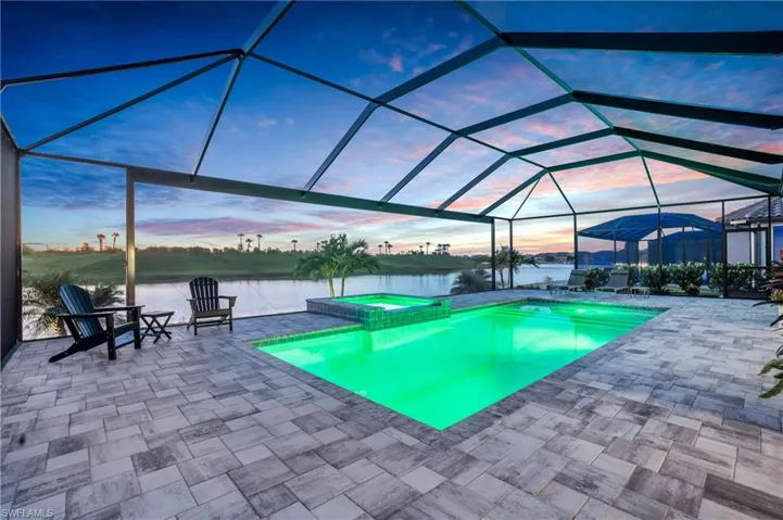 Pool at dusk featuring a water view, an in ground hot tub, a patio area, and a lanai