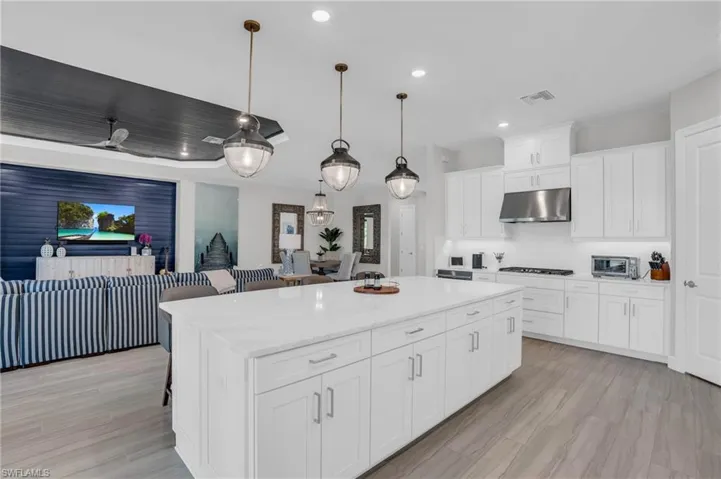 Kitchen featuring hanging light fixtures, backsplash, gas stovetop, white cabinets, and a kitchen island