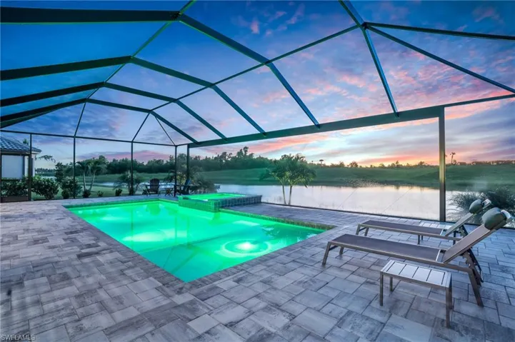 Pool at dusk with glass enclosure, a patio, a water view, and an in ground hot tub