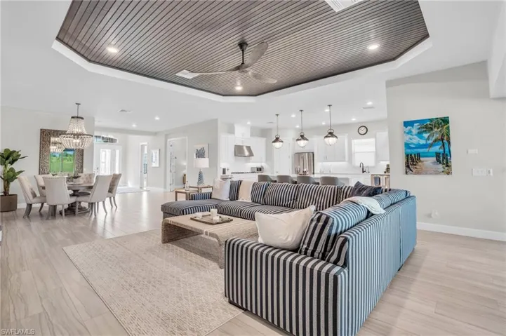 Living room featuring ceiling fan with notable chandelier, wooden ceiling, a tray ceiling, sink, and light wood-type flooring