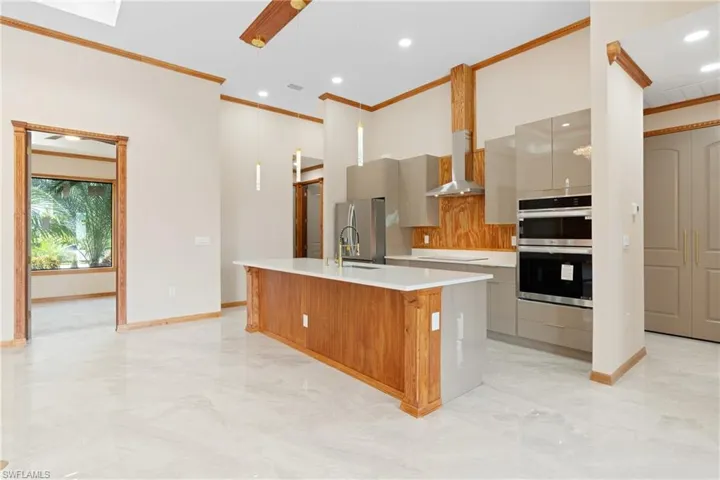 Kitchen featuring stainless steel appliances, wall chimney exhaust hood, a kitchen island with sink, and ornamental molding
