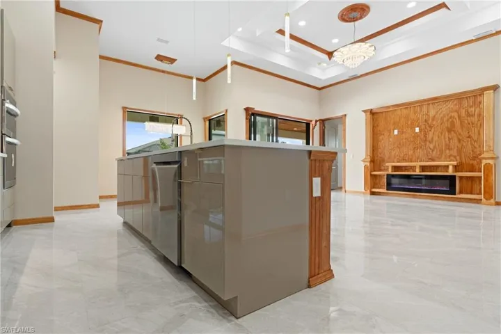 Kitchen featuring decorative light fixtures, light tile patterned flooring, a tray ceiling, ornamental molding, and a center island with sink