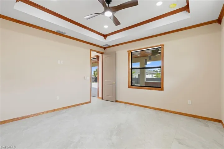 Tiled empty room with ceiling fan, crown molding, and a tray ceiling
