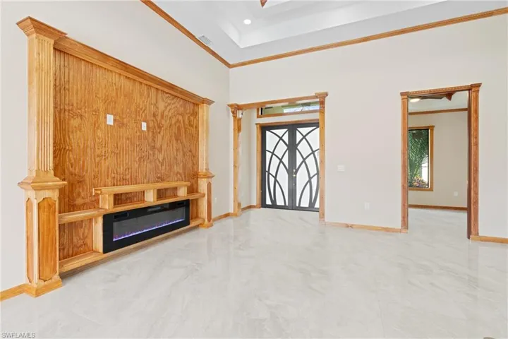 Unfurnished living room featuring crown molding, french doors, ornate columns, and light tile patterned floors