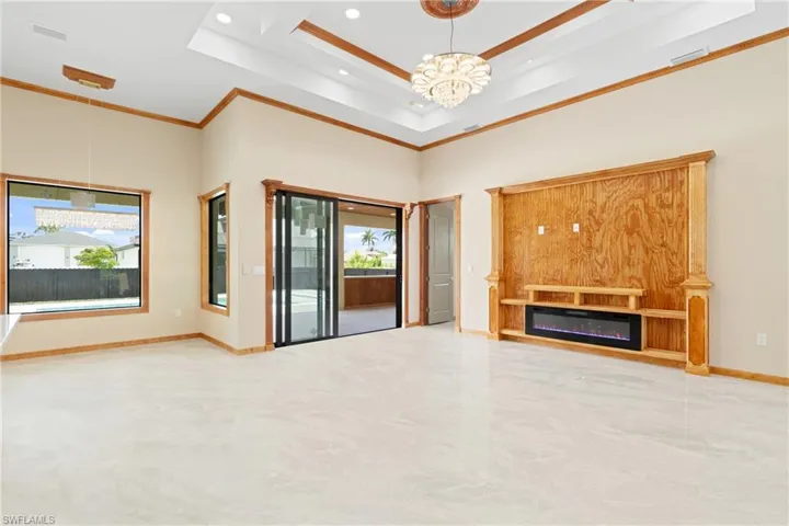 Unfurnished living room featuring ornamental molding, a wealth of natural light, a raised ceiling, and a chandelier