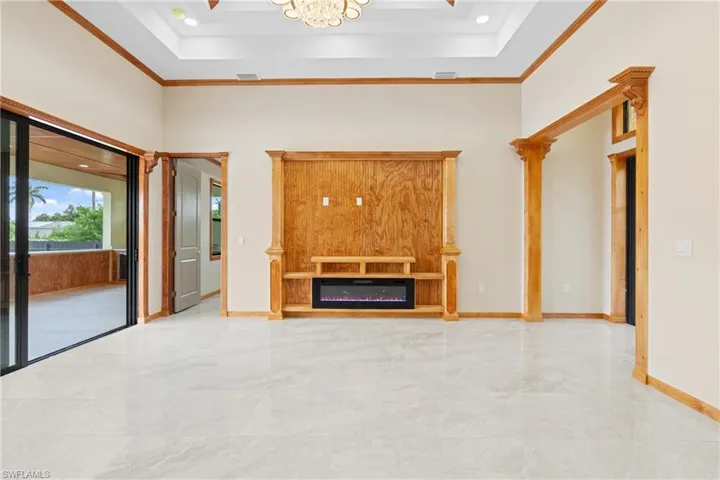 Unfurnished living room featuring a raised ceiling, light tile patterned floors, and ornamental molding