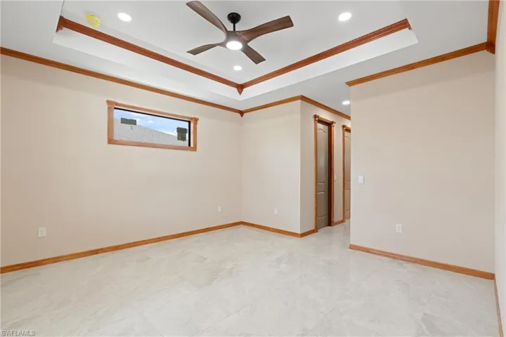 Empty room with crown molding, ceiling fan, a raised ceiling, and tile patterned floors