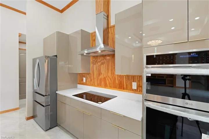 Kitchen featuring gray cabinets, wall chimney range hood, crown molding, appliances with stainless steel finishes, and light tile patterned floors