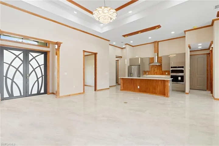 Kitchen with wall chimney range hood, stainless steel appliances, hanging light fixtures, french doors, and a center island with sink