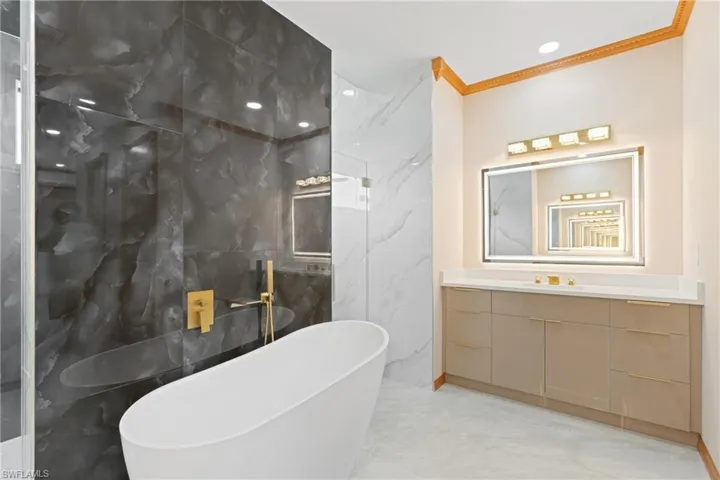 Bathroom with a bath, crown molding, vanity, tile walls, and tile patterned floors