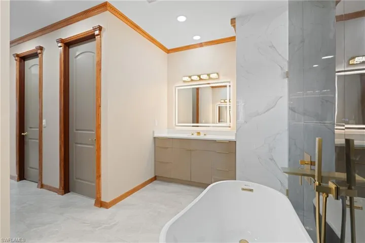 Bathroom with tile patterned flooring, a bath, vanity, and ornamental molding