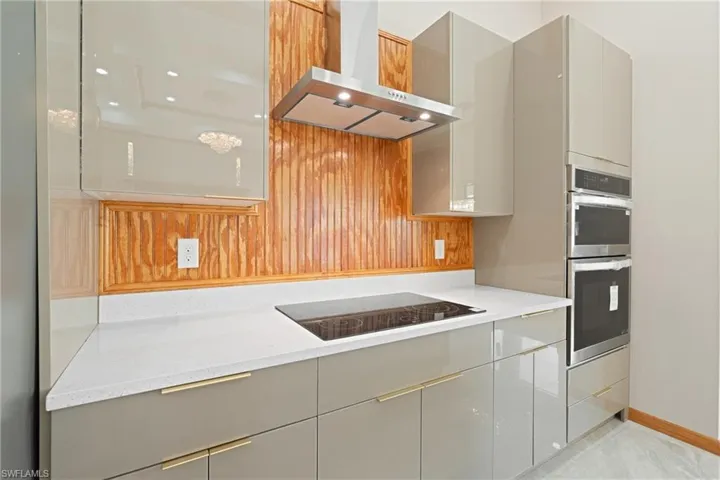 Kitchen featuring double oven, wall chimney range hood, gray cabinets, light tile patterned floors, and black electric stovetop