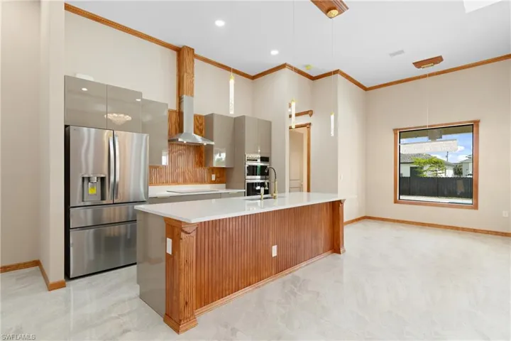 Kitchen featuring light tile patterned flooring, crown molding, a kitchen island with sink, wall chimney exhaust hood, and appliances with stainless steel finishes