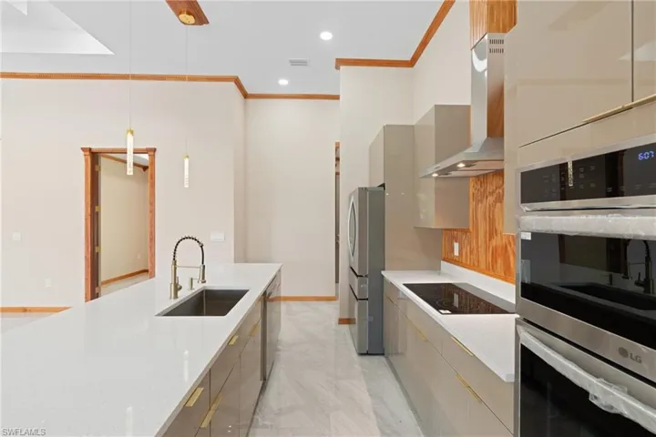 Kitchen with light tile patterned floors, appliances with stainless steel finishes, wall chimney exhaust hood, decorative light fixtures, and sink