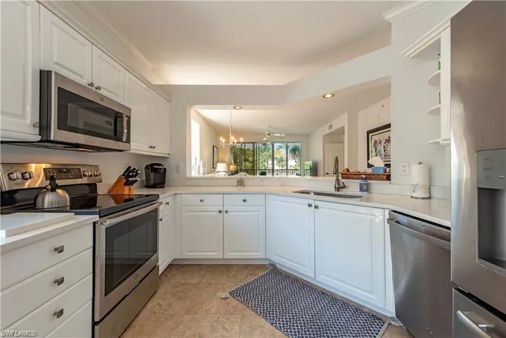 Kitchen with white cabinets, appliances with stainless steel finishes, a peninsula, light countertops, and a sink