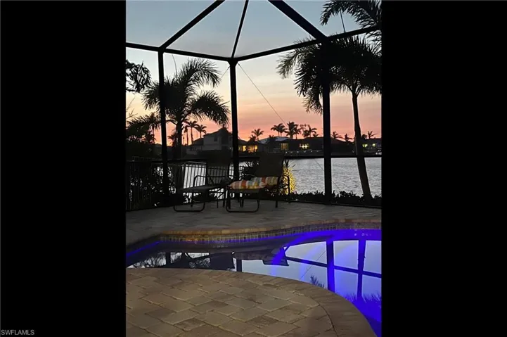 Pool at dusk with a patio, a water view, and a lanai