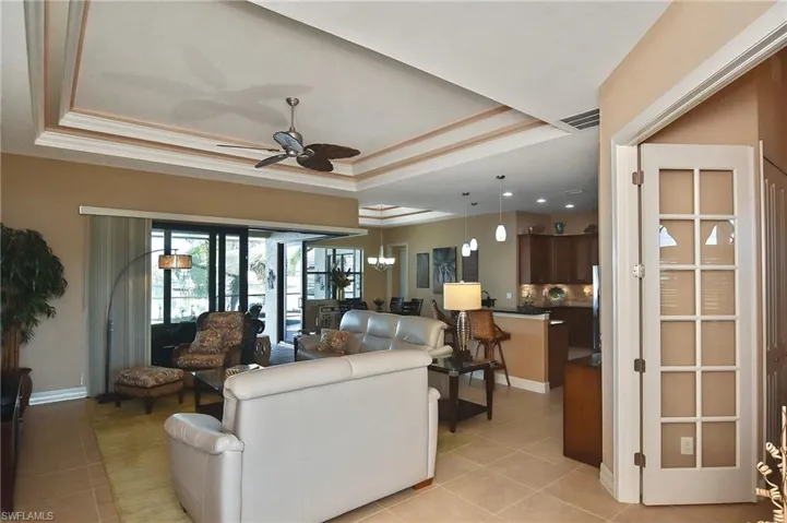Tiled living room featuring french doors, a tray ceiling, ceiling fan, and crown molding