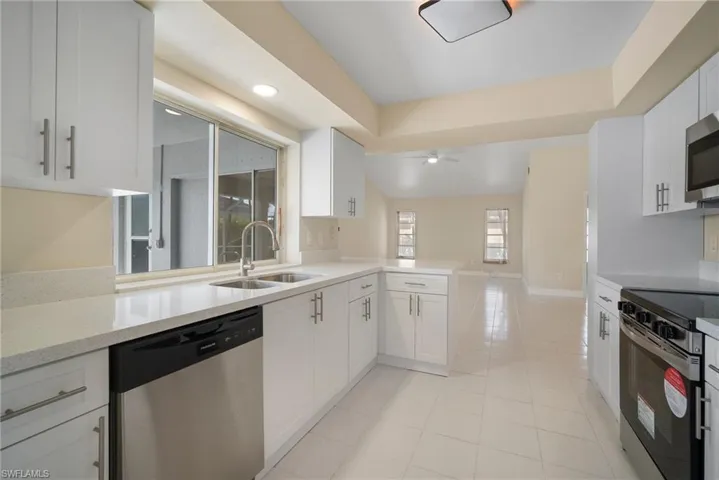 Kitchen with light tile patterned flooring, a sink, white cabinets, open floor plan, and appliances with stainless steel finishes