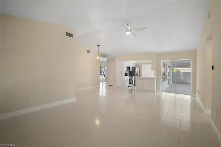 Unfurnished living room with lofted ceiling, ceiling fan, visible vents, and baseboards