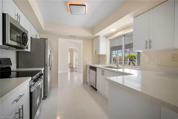 Kitchen featuring visible vents, white cabinets, light stone counters, stainless steel appliances, and a sink