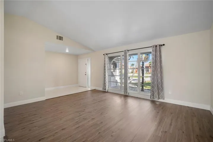 Unfurnished room featuring lofted ceiling, wood finished floors, visible vents, and baseboards