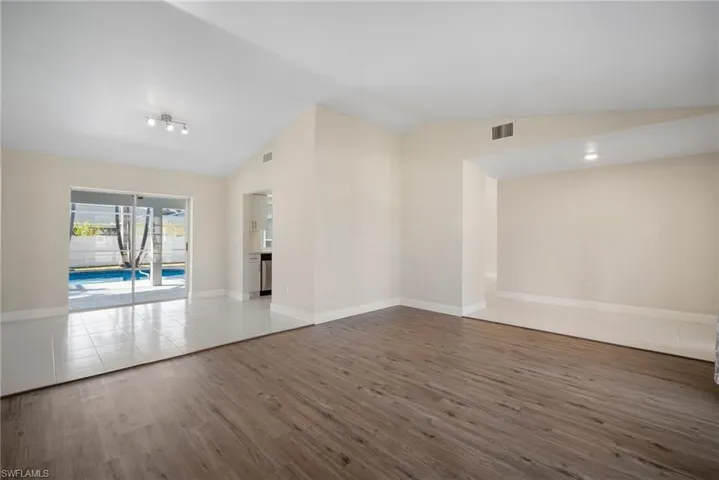 Empty room featuring vaulted ceiling, wood finished floors, visible vents, and baseboards
