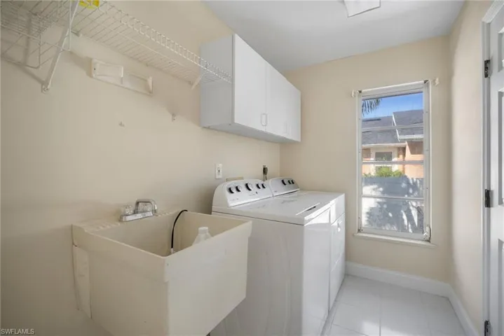 Clothes washing area featuring cabinet space, light tile patterned floors, baseboards, washing machine and clothes dryer, and a sink