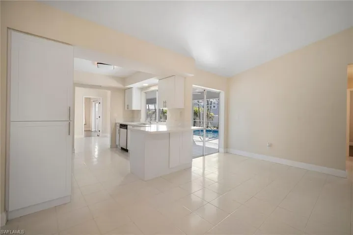 Kitchen featuring light countertops, stainless steel dishwasher, white cabinets, a peninsula, and baseboards