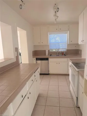 Kitchen with tile counters, electric range, dishwasher, and white cabinetry