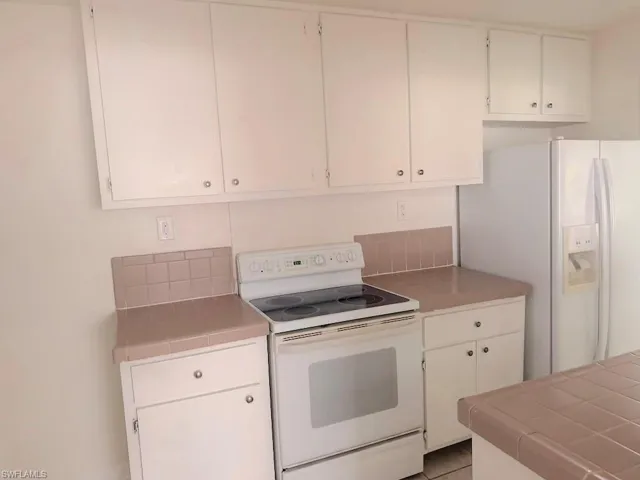 Kitchen with tile counters, white appliances, white cabinetry, and backsplash