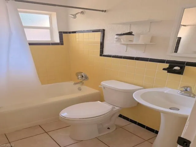Full bathroom with shower / tub combo with curtain, tile walls, wainscoting, light tile patterned floors, and a textured wall