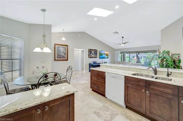Kitchen featuring sink, hanging light fixtures, vaulted ceiling with skylight, white dishwasher, and light stone countertops